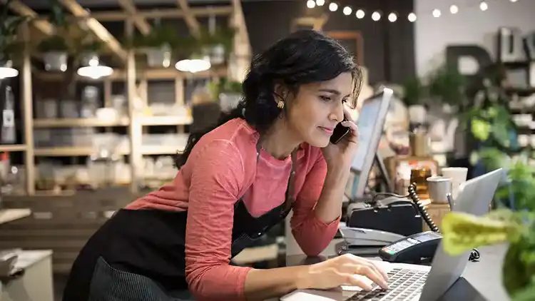 Žena hovoří na telefonu a používá notebook