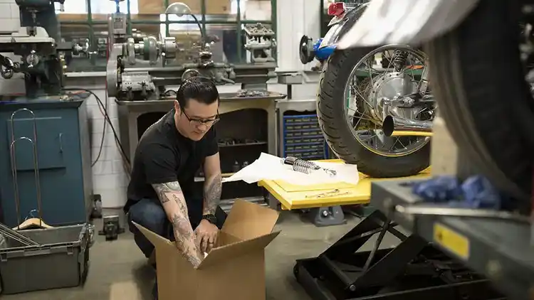 Eine Person in einer KFZ-Werkstatt bereitet ein schweres Paket für das Versenden vor