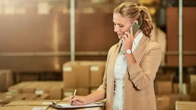 supervisor taking notes on a clipboard, talking on a mobile phone in a warehouse